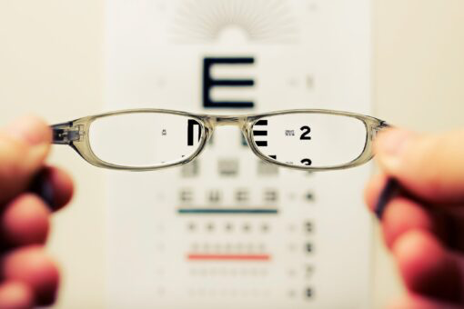 A person holding a pair of glasses in front of an eye chart.